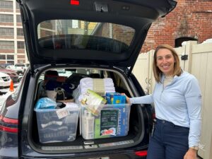 Woman standing in front of a car trunk with items to be donated.