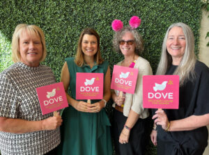group of women standing in front of a green wall holding signs that say Dove Recovery House for Women